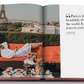 Open book featuring a man in a white robe lounging on an outdoor sofa at Plaza Athénée with a view of the Eiffel Tower, and an array of breakfast foods on a table. A quote about Paris appears on the right page, capturing the essence of French hospitality. The book is titled Plaza Athenee by Assouline.