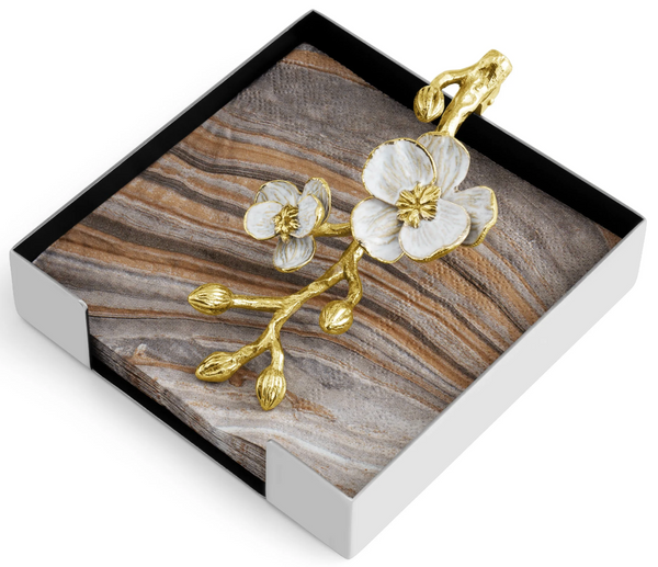 A Michael Aram Orchid Cocktail Napkin Holder with a wooden base featuring a golden brass branch with white flowers design, isolated on a white background.