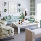 Bright living room with Green Greco Stripe pillows, green and beige furniture including a Highland House Barrow Sofa, patterned armchairs, white coffee table, leafy artwork, two table lamps, and a large window for extra light.