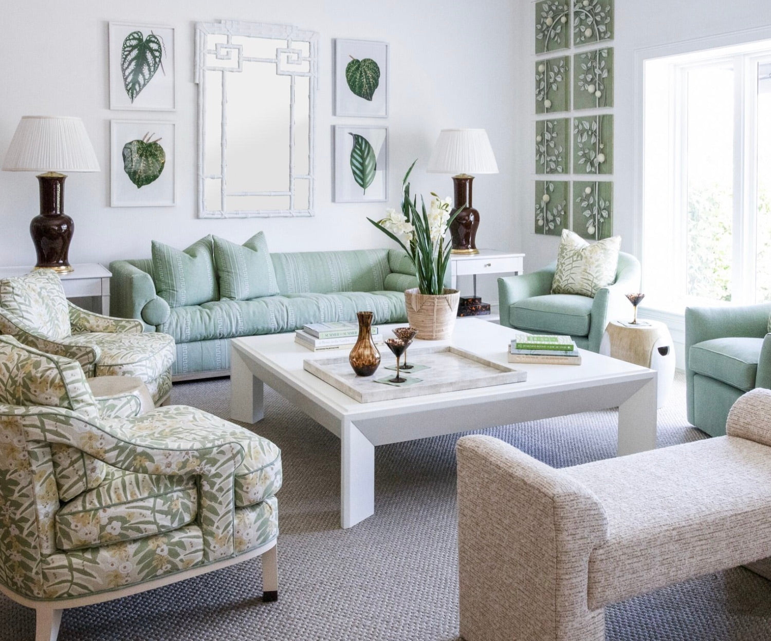 Bright living room with Green Greco Stripe pillows, green and beige furniture including a Highland House Barrow Sofa, patterned armchairs, white coffee table, leafy artwork, two table lamps, and a large window for extra light.