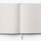 The Riffle Paper Co. Blue Hydrangea Desk Accessory Collection features an open notepad with a blank left page, lined right page, and light blue ribbon bookmark—an elegant addition to your workspace.