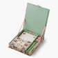The Dahlia Collection by Riffle Paper Co. is a floral stationery set with writing paper, envelopes, a gold pen, and two pink wax seals, all arranged in an open decorative box with a light green interior.