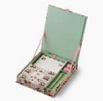 The Dahlia Collection by Riffle Paper Co. is a floral stationery set with writing paper, envelopes, a gold pen, and two pink wax seals, all arranged in an open decorative box with a light green interior.