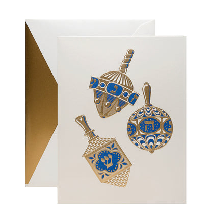 The Crane Engraved Spinning Dreidels Box Set includes Hanukkah cards with gold and blue dreidels on pearl white cardstock, paired with matching white envelopes lined in gold.