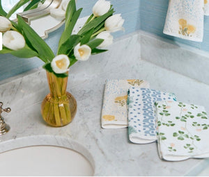 A vase with white tulips and three Weezie x Lulie Wallace Beth Powder Bath Towels by Weezie Towels in absorbent terry sit on a marble bathroom countertop beside the sink.