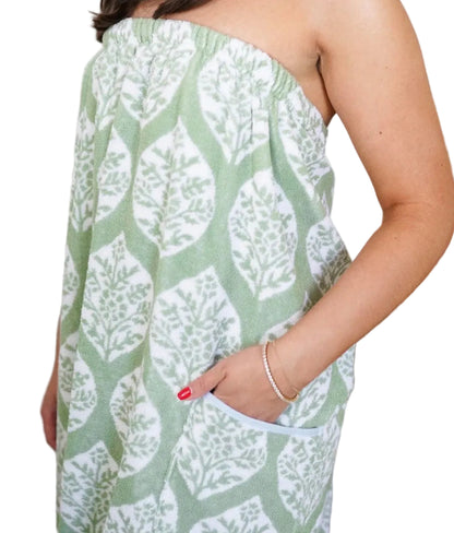 Person wears the Weezie Towels Ivy Block Towel Wrap, a green and white leafy design with an elastic back and pocket for a comfy, hands-free fit; only torso and one arm are shown.