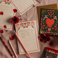 Flat lay of the Rifle Paper Co. Valentine's Day card, Juliet Checklist Notepad, illustrated notepads, pencils, matches, red flower petals, and a handwritten to-do list on a pink surface.