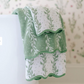 Two towels from the Willow Scallop Towel Collection by Weezie Towels, featuring green and white scalloped edges, are draped over a white toilet, lending a spa-like touch to the bathroom.