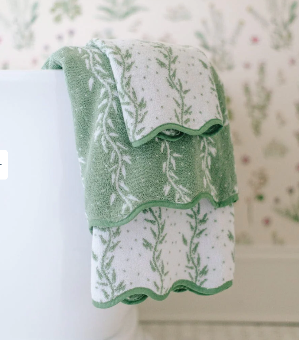Two towels from the Willow Scallop Towel Collection by Weezie Towels, featuring green and white scalloped edges, are draped over a white toilet, lending a spa-like touch to the bathroom.