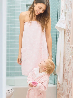 A woman in a Weezie Towels Pink Hearts Towel Wrap smiles at a small child in a matching pink robe as they face each other in the bathroom.