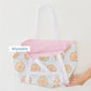 A hand holds the Weezie x Lulie Wallace Beach Tote by Weezie Towels, featuring a Savannah print, white straps, and a pink interior. A "Wipeable" label is displayed on the image.