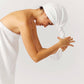 A person leans forward, twisting a Weezie Towels Hair Towel Wrap around their head while wearing a matching white towel.