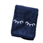 The Weezie Towels Makeup Towel is a navy terry towel with closed eyes and eyelashes embroidered in white, designed to be stain resistant for makeup removal.