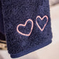 Close-up of Weezie Towels Makeup Towel in navy terry, featuring two pink heart outlines embroidered on its stain resistant fabric.