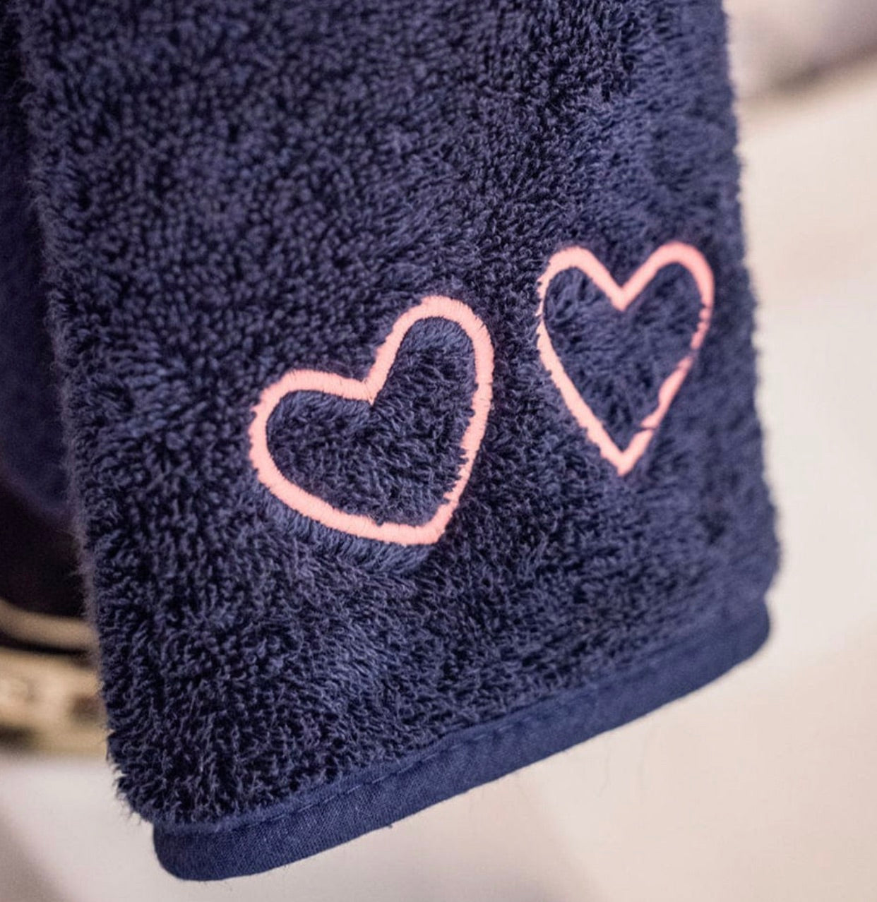 Close-up of Weezie Towels Makeup Towel in navy terry, featuring two pink heart outlines embroidered on its stain resistant fabric.
