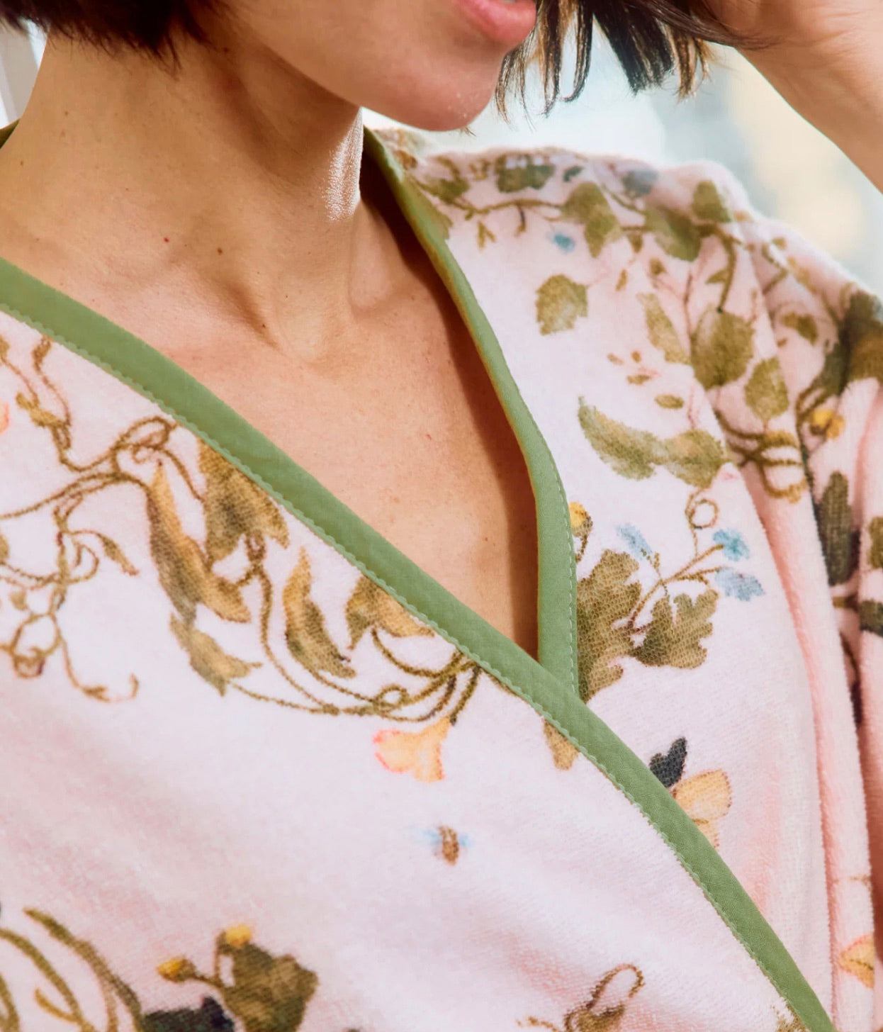 A person wearing the Vivian Cherry Blossom Robe by Weezie Towels, a soft pink floral velour robe with green trim and bell sleeves, photographed from the neck down.
