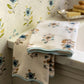 Two folded Floral Scallop Cora Towels from HIVE Home, Gift and Garden rest on a white countertop beside a tray with a brush and soap, bringing a touch of luxury to your bathroom space.