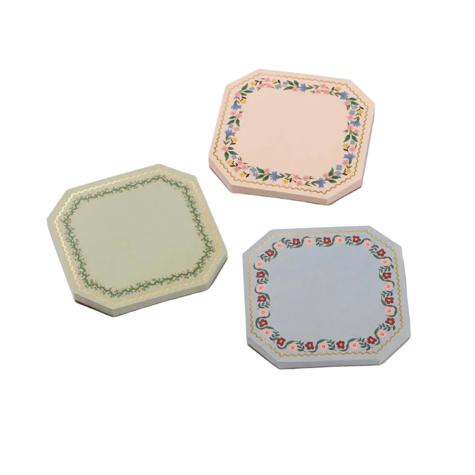 The Gemma Mini Notepad Trio by Rifle Paper Co. includes three octagonal notepads in pastel pink, green, and blue with floral borders and gold details. Each pad has tear-off sheets, ideal for notes on a white background.