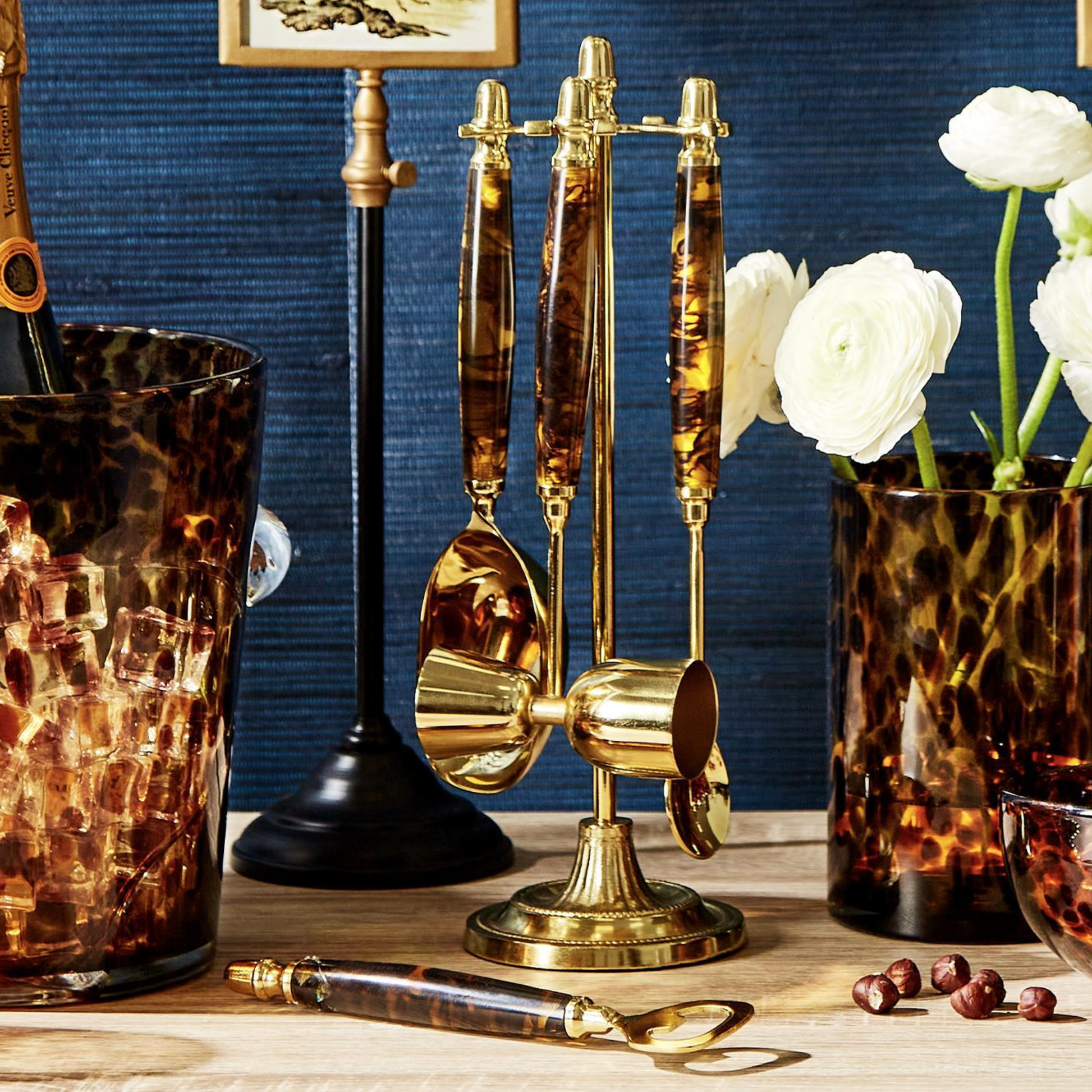 The Two's Company Tortoise Bar Set with gold accents sits on a wooden surface, complemented by matching barware and white flowers—an ideal addition to any cocktail lover’s home bar.