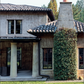 Two-story stucco house with tile roof, covered porch supported by columns, tall chimney draped in climbing ivy, and a green lawn in front—a classic example of Southern homes reminiscent of those featured in *Creating Home: Design for Living* by Rizzoli.
