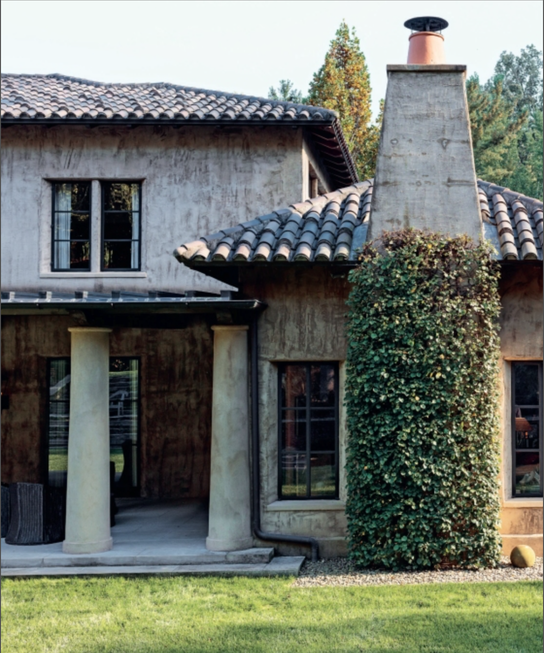 Two-story stucco house with tile roof, covered porch supported by columns, tall chimney draped in climbing ivy, and a green lawn in front—a classic example of Southern homes reminiscent of those featured in *Creating Home: Design for Living* by Rizzoli.