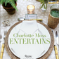 A place setting with a woven charger, crisp white napkin, and refined cutlery captures the spirit of gracious hospitality. At each seat, the Charlotte Moss Entertains plate by Rizzoli sets an elegant tone. Lush greenery, a softly glowing candle, and personalized name cards complete the inviting tablescape.