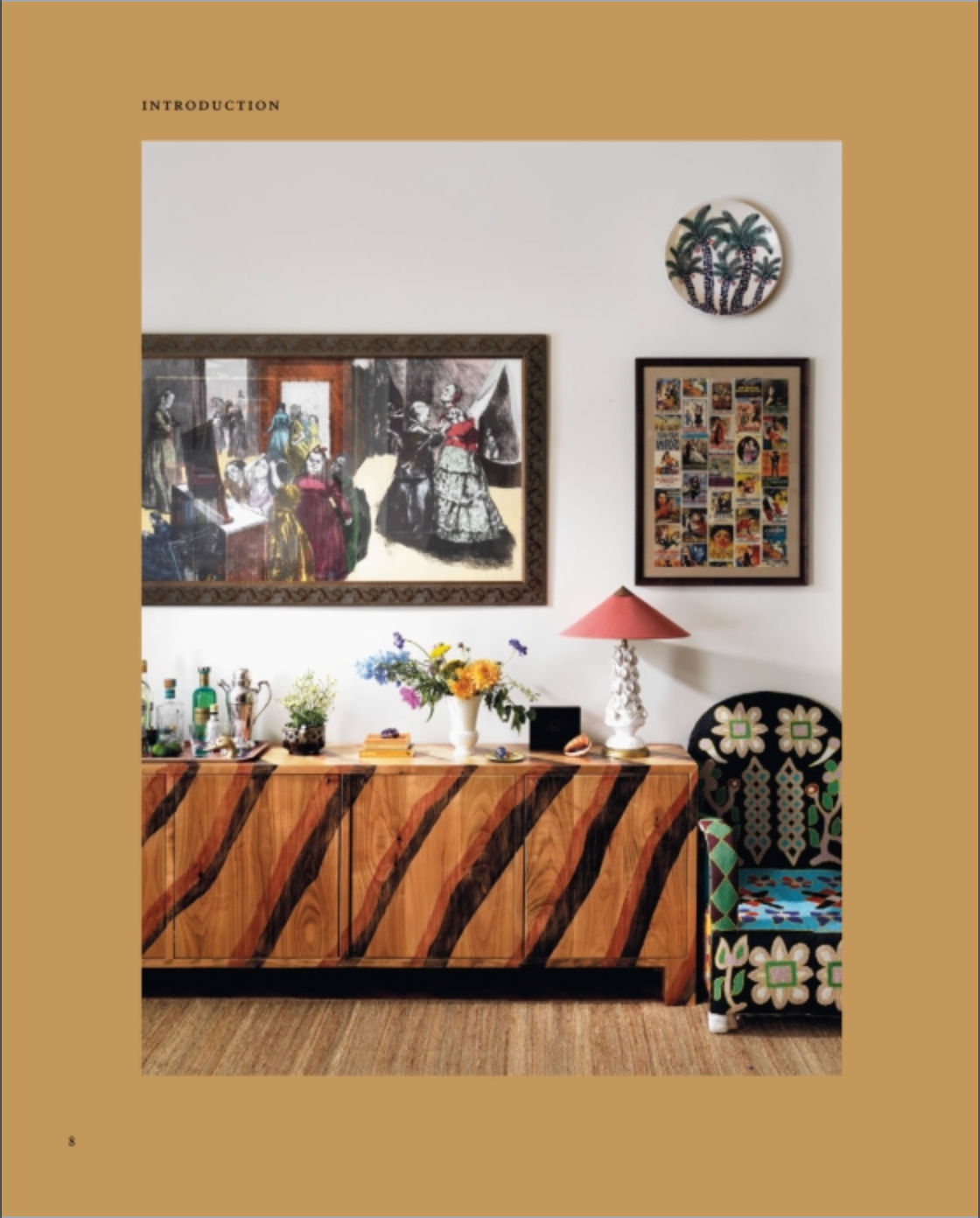 Featuring “Beata Heuman, Every Room Should Sing” by Rizzoli, this space showcases a wooden sideboard with a zebra pattern adorned with flowers and a lamp, infusing the room with Scandinavian flair; vibrant art and photos hang above, beside an upholstered floral chair thoughtfully arranged by an interior designer.