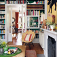 A cozy living room with bookshelves, a chair, a fireplace, and a green tray atop a velvet sofa featuring bespoke furnishings from Beata Heuman’s Every Room Should Sing (Rizzoli); the subtly Scandinavian-styled dining room is seen through glass doors.