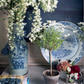 Elevate your home decor with a stylish tabletop display featuring A Home For All Seasons by Penguin Random House, paired with a large blue-and-white vase of white flowers, a small potted plant, a plate, assorted flowers in jars, and curated accents—perfect for entertaining in style.