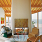 Experience true interior design authority for unique homes with inspiration from AD At Home: Architectural Digest by Penguin Random House, featuring modern living spaces with tall white fireplaces, wicker chairs, round tables, patterned pillows, and breathtaking ocean views through expansive windows.