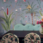 Dining table with floral chairs and a pale blue scalloped bench against de Gournay: Hand-Painted Interiors wallpaper featuring trees, flowers, and a brass wall lamp.