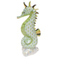 The Herend Sea Horse is a porcelain figurine featuring hand-painted designs, a green scale pattern, gold accents on its tail, fins, and horn, plus a glossy finish. It stands upright on a reflective surface.