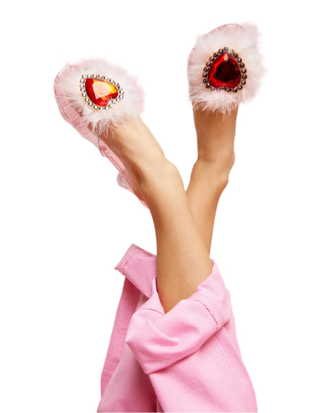 Close-up of a person wearing pink pants and Super Smalls' Daydream Queen Play Shoes, which are fuzzy slippers decorated with large, heart-shaped gems, their legs crossed and raised in a fun dress-up debut.