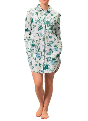 A person stands barefoot wearing the Matouk Luca Palmyra Emerald Sleep Shirt—an oversized, long-sleeve, button-up pajama top with a green and blue floral and leaf print.