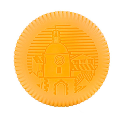 A round, orange biscuit with an embossed clock tower and buildings, inspired by Baobab’s Saint Tropez Body Wellness Collection and the lively summer essence of southern France.