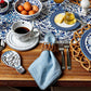 A breakfast table features eggs, coffee, butter, honey, berries, blue-patterned dishes, silverware, and a Juliska Berry Trim Napkin from the Berry Trim Napkin Collection atop a wooden table.