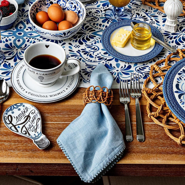 A breakfast table features eggs, coffee, butter, honey, berries, blue-patterned dishes, silverware, and a Juliska Berry Trim Napkin from the Berry Trim Napkin Collection atop a wooden table.