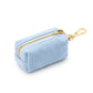 The Foggy Dog Waste Bag Dispenser in Blue Chambray is a chic, light blue rectangular fabric pouch featuring a gold zipper and an attached gold metal clip; shown on a white background, this elegant accessory keeps pet waste bags stylishly at hand.