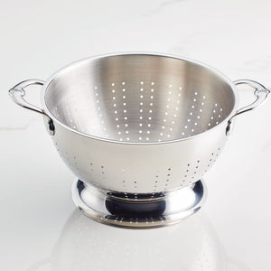 The Hestan Provisions Stainless Steel Colander 2-Piece Set, featuring ergonomic handles for comfort and superior drainage, rests on a white surface.
