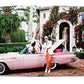 A man stands in front of a pink convertible with the trunk open, positioned beside a woman who is sitting on the car. In the backdrop, an elegant house designed by Martyn Lawrence Bullard and lush greenery paint a picture of ultimate luxury worthy of celebrity homes, featuring Star Style: Interiors of Martyn Lawrence Bullard by Vendome.