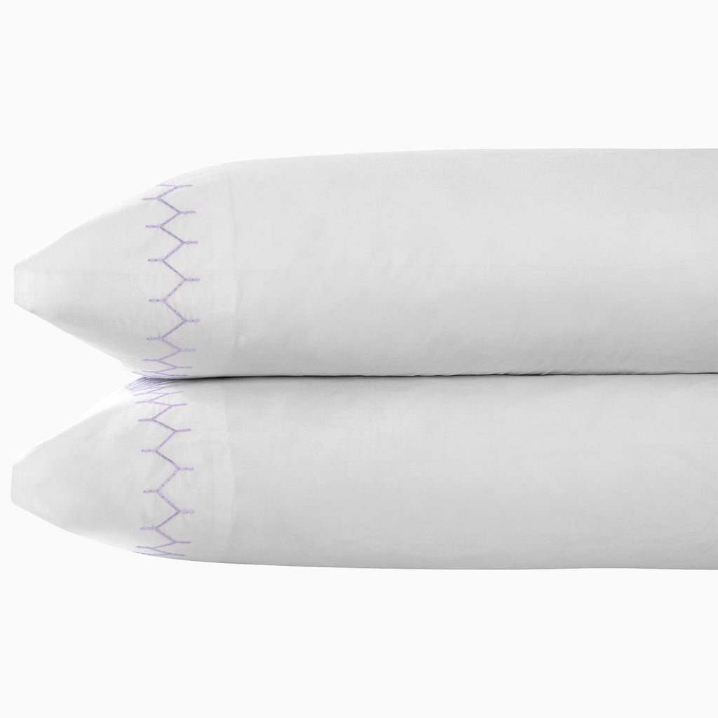 Two stacked white pillows with purple zigzag stitching on the edges, crafted from John Robshaw Stitched Sheet Set in Lavender organic cotton percale, set against a plain background.
