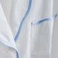 Close-up of the Sue Nightshirt by Haute Home, a luxury white cotton sateen sleepwear piece featuring blue piping on the pocket and edges for an elegant look.