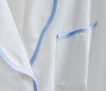 Close-up of the Sue Nightshirt by Haute Home, a luxury white cotton sateen sleepwear piece featuring blue piping on the pocket and edges for an elegant look.