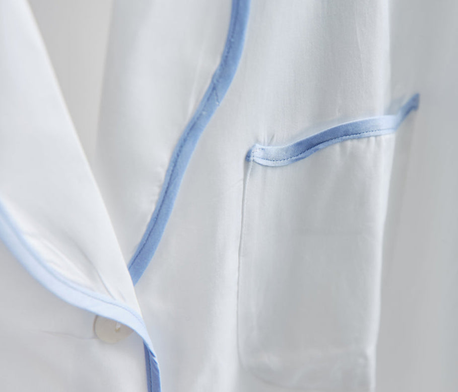 Close-up of the Sue Nightshirt by Haute Home, a luxury white cotton sateen sleepwear piece featuring blue piping on the pocket and edges for an elegant look.
