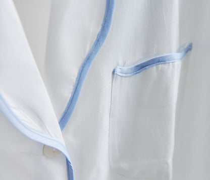 Close-up of the Sue Nightshirt by Haute Home, a luxury white cotton sateen sleepwear piece featuring blue piping on the pocket and edges for an elegant look.