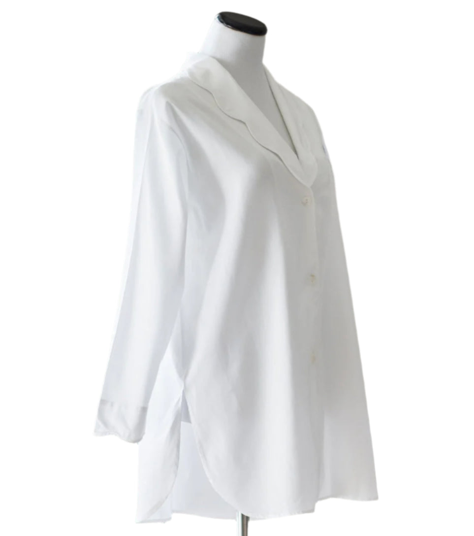 The Sue Nightshirt by Haute Home is a white, long-sleeve button-up blouse in smooth cotton sateen with a curved collar and side slits, shown on a dress form—an elegant choice for luxury sleepwear.