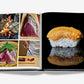 The Assouline book "Sushi Shokunin: Japan's Culinary Masters" features an open spread showing sushi masters at work on the left page and a close-up of orange-topped sushi on the right, all set against a black background.