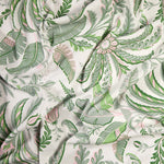A close-up of the Addison Ross Palm Beach Tablecloth, crafted from luxury cotton-linen with a green and pink botanical print of leaves and flowers on white. Slight wrinkles add texture to this elegant table linen.