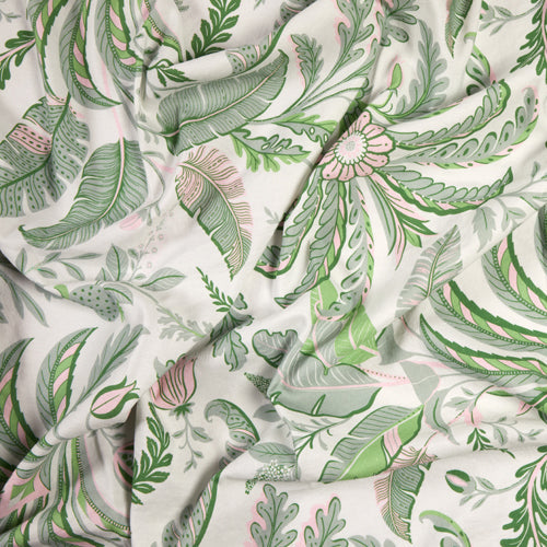 A close-up of the Addison Ross Palm Beach Tablecloth, crafted from luxury cotton-linen with a green and pink botanical print of leaves and flowers on white. Slight wrinkles add texture to this elegant table linen.