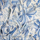 The Palm Beach Tablecloth by Addison Ross features crumpled white fabric with blue botanical and leaf patterns in various shades, adding intricate detail and a touch of elegance to any table setting.